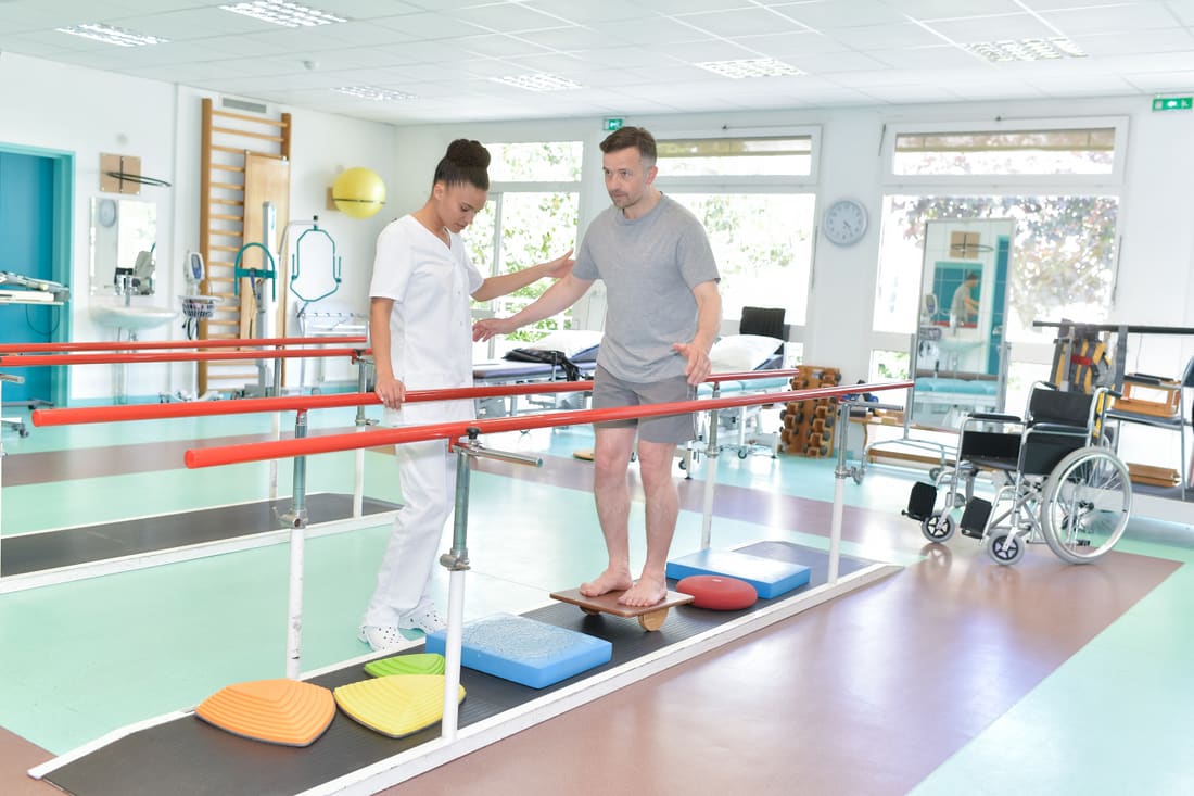 A physiotherapist helping a man walk between parallel bars